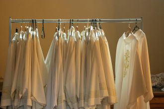 Row of white liturgical robes hanging in a church interior, bathed in soft lighting.