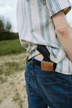 A young man outdoors with a gun tucked into his belt, captured from behind.